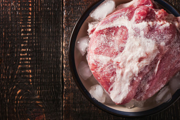 Frozen pork on the plate with ice on the wooden table