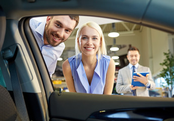 happy couple with car dealer in auto show or salon