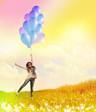 Happy girl flying with balloons on sunny summer meadow.