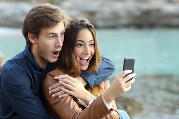 Shocked couple watching a smart phone on holidays