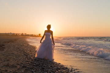 Young bride enjoys walking on a hazy beach at dusk.