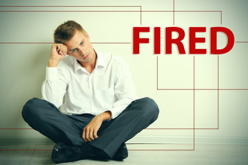 Sad fired office worker sitting on floor on wall background