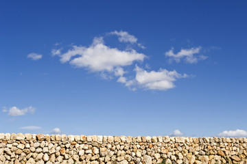 Rural stone wall and blue sky with white clouds as background