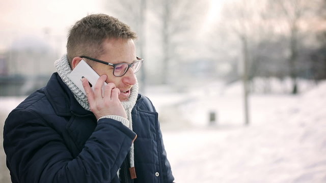 Happy man talking on cellphone in the park at winter time 