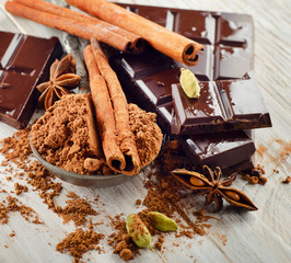 Broken chocolate bar and cocoa powder on a wooden board.