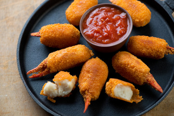 Close-up of a frying pan with breaded crab claws and dip sauce