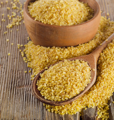 Bulgur in a wooden spoon on a  wooden background. Selective focu