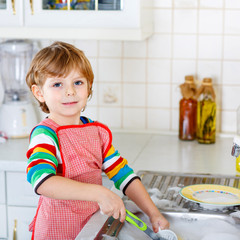 Funny kid boy helping and washing dishes at home