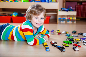 Funny little boy playing with lots of toy cars indoor