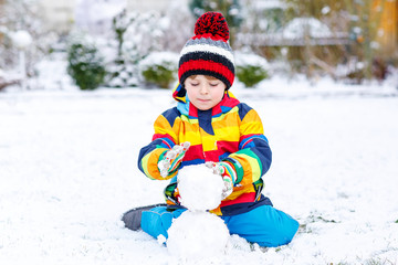 Fototapeta na wymiar Funny preschool boy in colorful clothes making a snowman