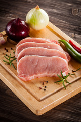 Raw pork chops on cutting board and vegetables