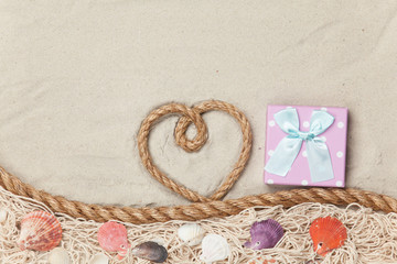 Fototapeta na wymiar Gift box and rope in heart shape near net and shells