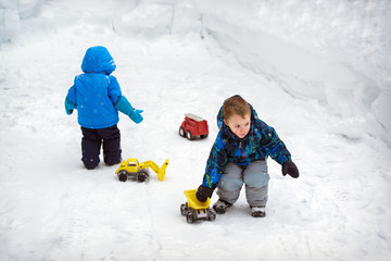 Fototapeta na wymiar Two Boys Playing in Deep Snow with Trucks