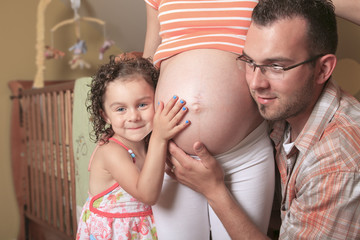 Little cute girl looking at her mother pregnant tummy