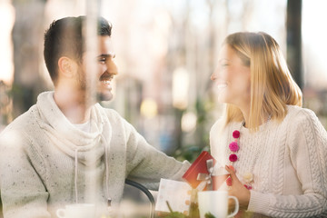 Happy young couple sitting in a restaurant opening the gift
