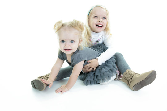 Two cute little blond sisters kneeling on the floor arm in arm c