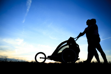 Obraz na płótnie Canvas Silhouettes of parents loving their child in a stroller