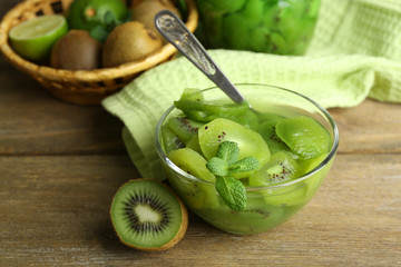 Tasty kiwi jam in glass bowl and jar on wooden background