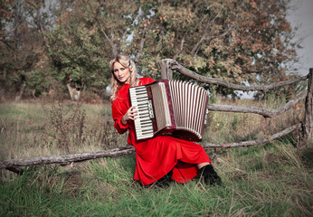 Retro woman in traditional costume with an accordion, in a field