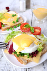 Toast with egg Benedict and tomato on plate on wooden table