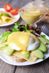 Toast with egg Benedict and avocado on plate on wooden table