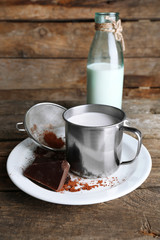 Metal mug and glass bottle of milk with chocolate chunks and