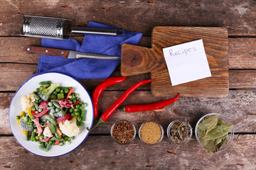 Frozen vegetables and blank notebook, on wooden table