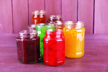 Homemade jars of fruits jam on color wooden background