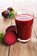 Glass of beet juice with beets on wooden table close up