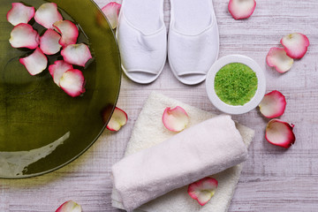 Obraz na płótnie Canvas Spa bowl with water, rose petals, towel and slippers