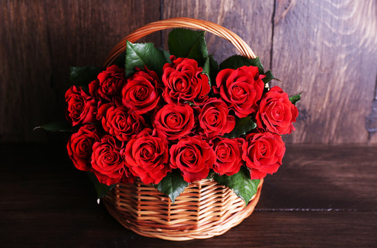 Bouquet of red roses in basket on wooden background