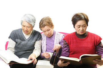 分厚い本を読んで勉強している高齢者のおばあさん3人組