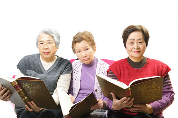 分厚い本を読んで勉強している高齢者のおばあさん3人組