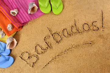 Fototapeta na wymiar The word Barbados written in sand on a beach with towel flip flops seashells summer vacation holiday photo