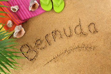 Fototapeta na wymiar The word Bermuda written in sand on a beach with towel flip flops seashells summer vacation holiday photo