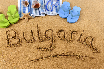 The word Bulgaria written in sand on a beach with towel flip flops seashells summer vacation...