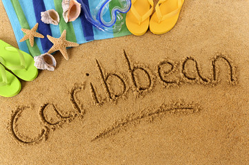 The word Caribbean written in sand on a beach with towel flip flops seashells summer vacation holiday photo