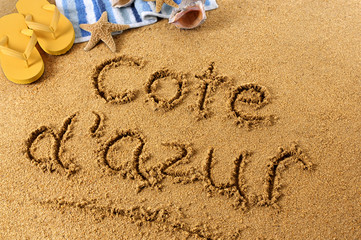 The word Cote dAzur written in sand on a beach with towel flip flops seashells France summer...