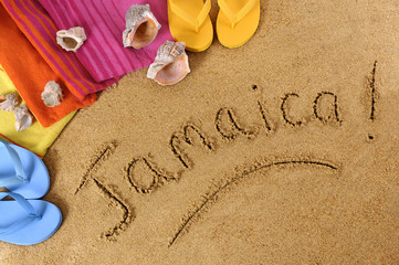 Fototapeta na wymiar The word Jamaica written in sand on a beach with towel flip flops seashells Caribbean summer vacation holiday photo