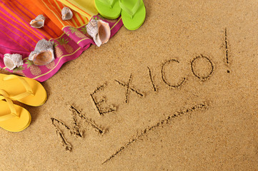 Fototapeta na wymiar The word Mexico written in sand on a beach with towel flip flops seashells Mexican summer vacation holiday photo