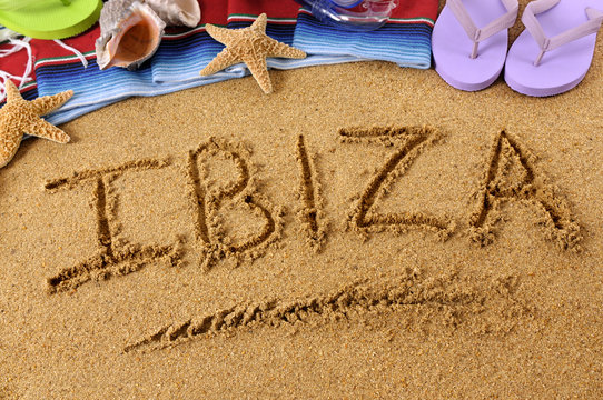 The word Ibiza written in sand on a beach with towel flip flops seashells summer vacation holiday photo
