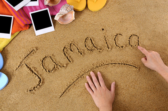 Child hands writing the word Jamaica written in sand on a beach with towel flip flops seashells Caribbean summer vacation holiday photo
