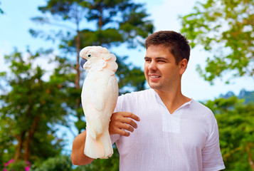 young man, ornithologist holding gorgeous cockatoo parrot