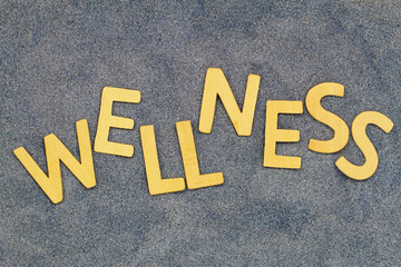 Wellness written with wooden letters on blue sand