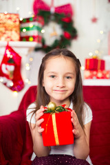 Fototapeta na wymiar Little girl sitting on couch holding red box, gift, Christmas