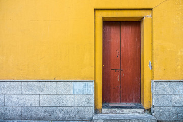 Vintage building with red wooden door and yellow concrete wall