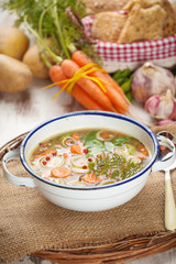 Vegetable soup in a metal bowl on a rural rustic wooden table.
