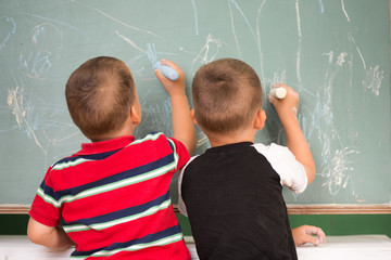 Two little boys drawing with chalk on a chalkboard