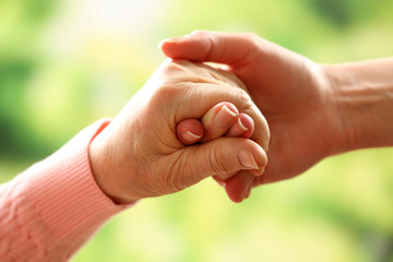 Old and young holding hands on light background, closeup
