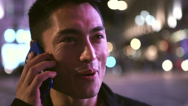 Young asian man laughing on his phone at night in the city